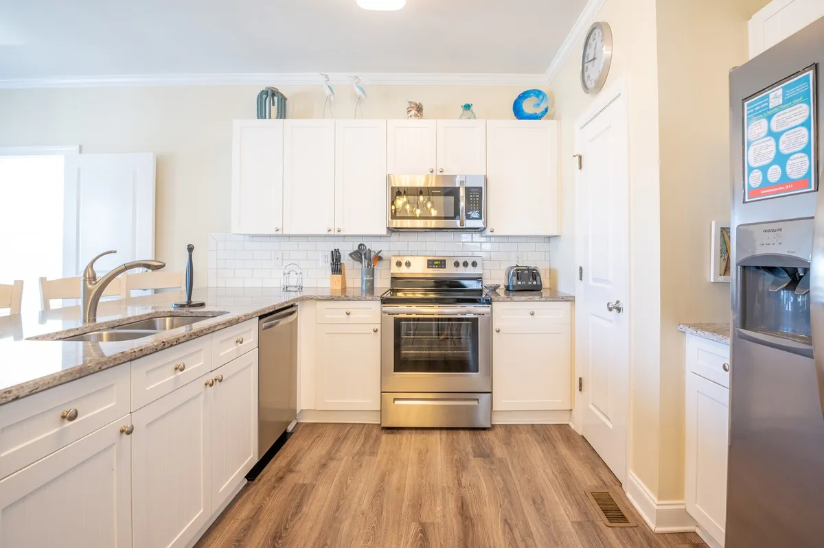 A modern kitchen with gleaming granite countertops, stainless steel appliances, white cabinetry, and a central island with bar stools. The layout encourages both cooking and casual conversation, with the island seating serving as a spot for morning chats or quick meals.