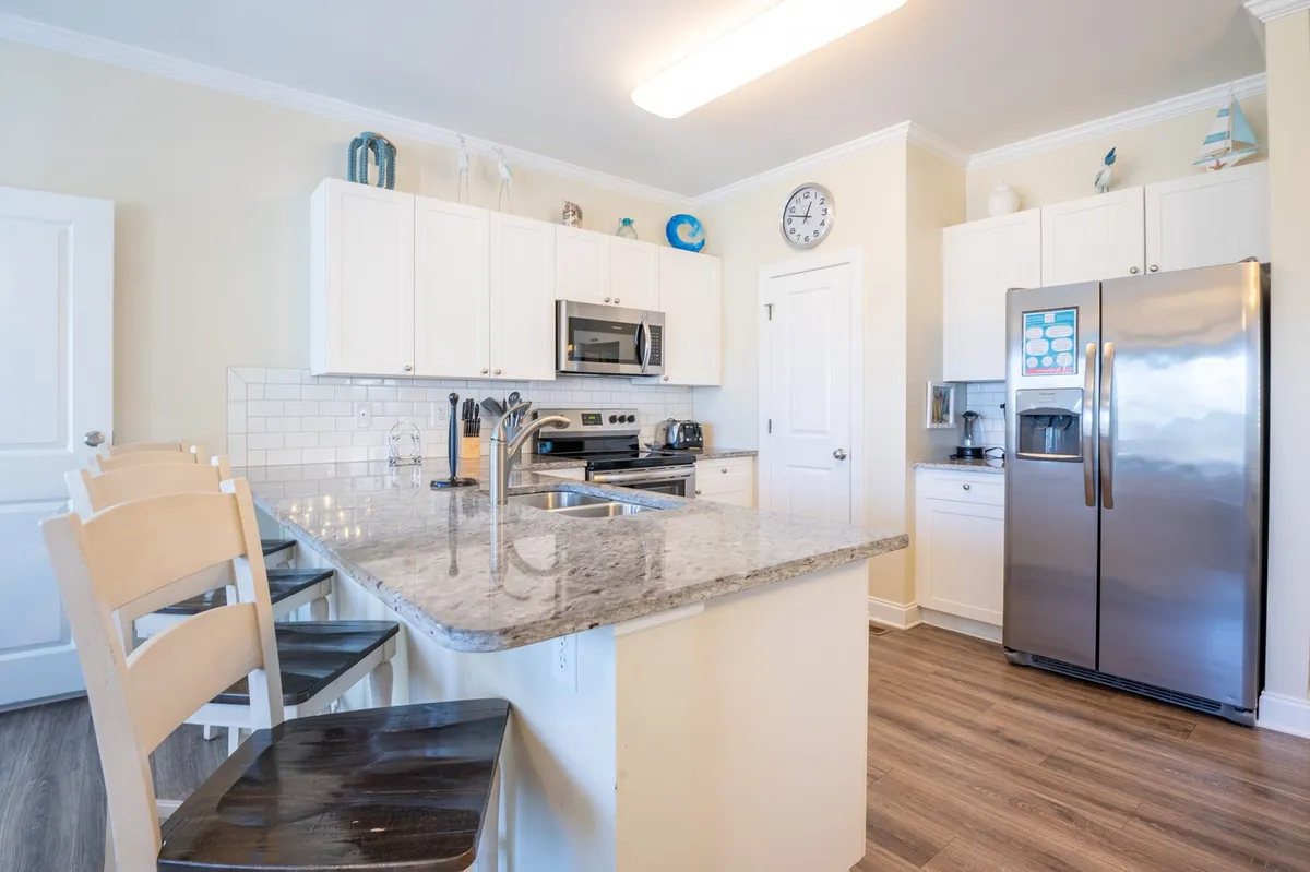 A modern kitchen with granite countertops, stainless steel appliances, white cabinetry, and bar stools. The space is bright and functional, ideal for group cooking, entertaining, and shared meals.