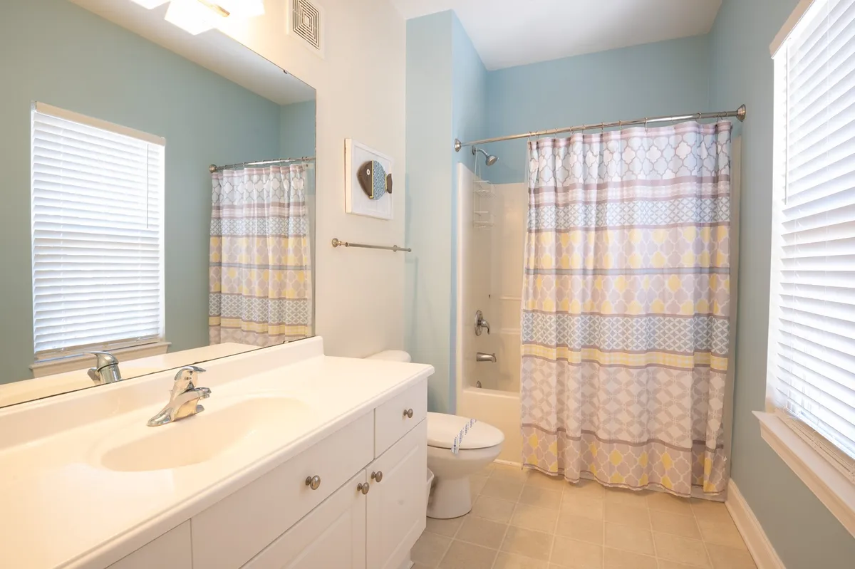 A spa-inspired bathroom featuring a vanity sink, mirror, window for natural light, and a shower curtain enclosing the bathing area. The space is clean, serene, and designed for relaxation and rejuvenation.