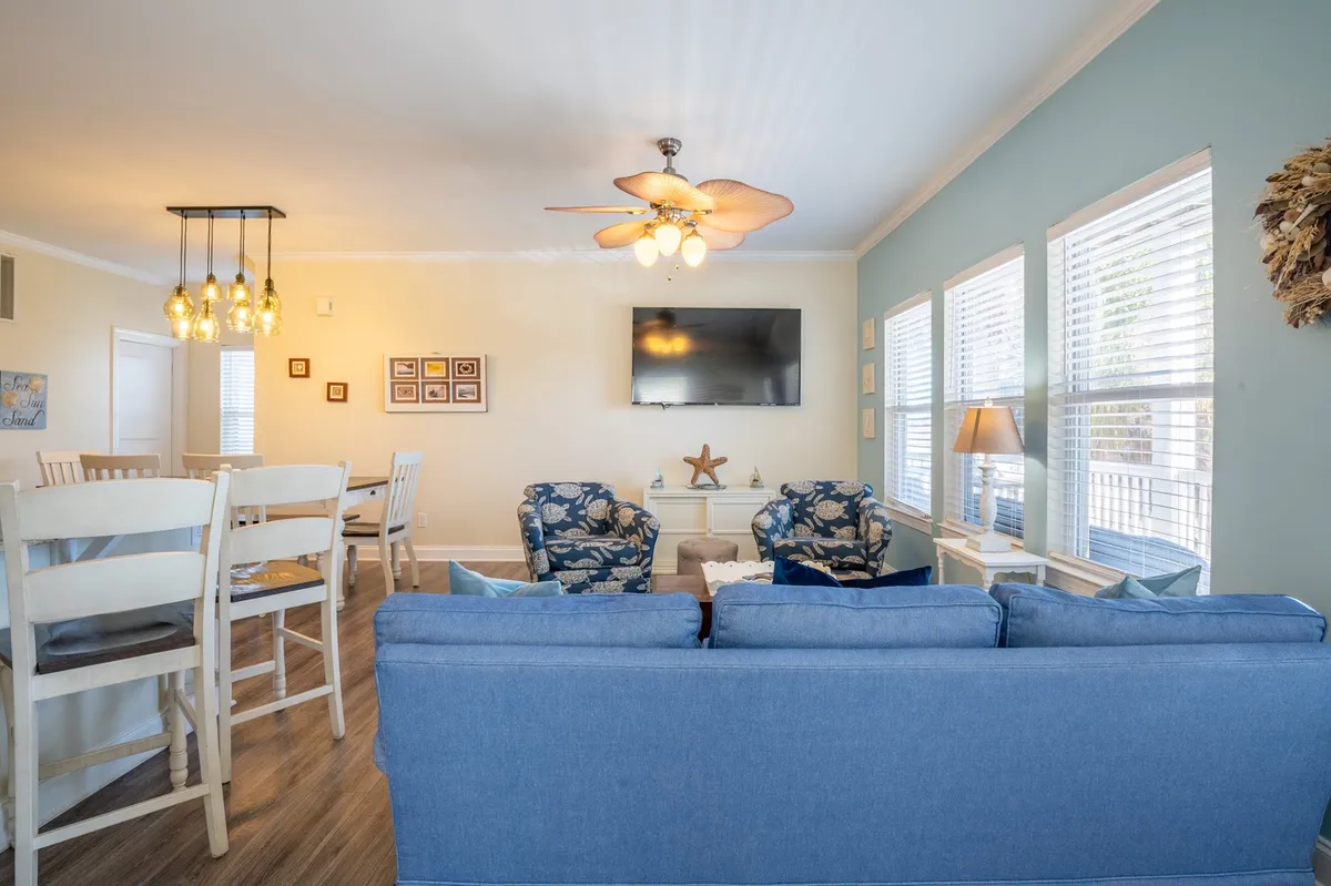 The open-concept living area is styled with a comfortable sofa, decorative chairs, a modern light fixture, and wall art. The setup is inviting and supports group activities like movie nights, relaxed socializing, and quiet reading sessions.